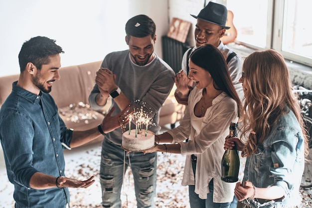 Buon compleanno! Vista dall'alto di un giovane felice che festeggia il compleanno tra amici mentre si trova nella stanza con i coriandoli che volano in giro