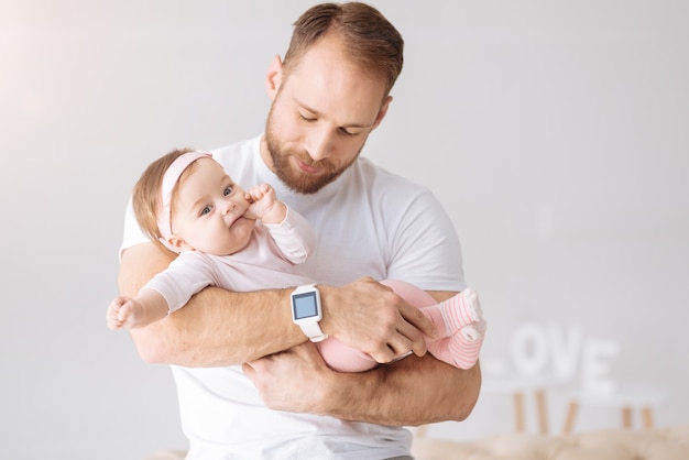 Buon fine settimana. Affascinante bella bambina carina sdraiata nelle mani del padre e distoglie lo sguardo mentre esprime interesse e gioia