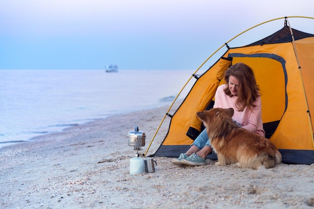 Buon fine settimana al mare - ragazza con un cane in tenda sulla spiaggia all'alba. Paesaggio ucraino al Mar d'Azov, Ucraina