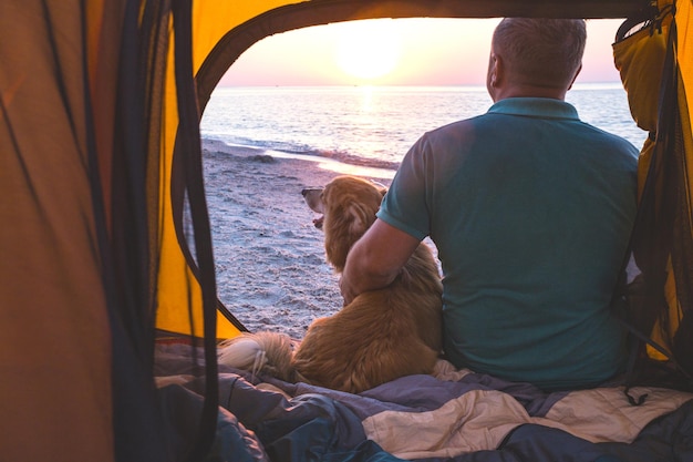 Buon fine settimana al mare - uomo con cane in tenda sulla spiaggia all'alba. Paesaggio ucraino al Mar d'Azov, Ucraina