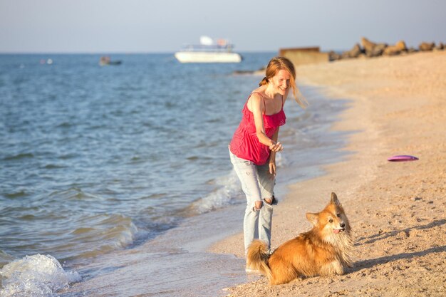 Buon fine settimana divertente al mare - ragazza che gioca al frisbee con un cane sulla spiaggia. Estate