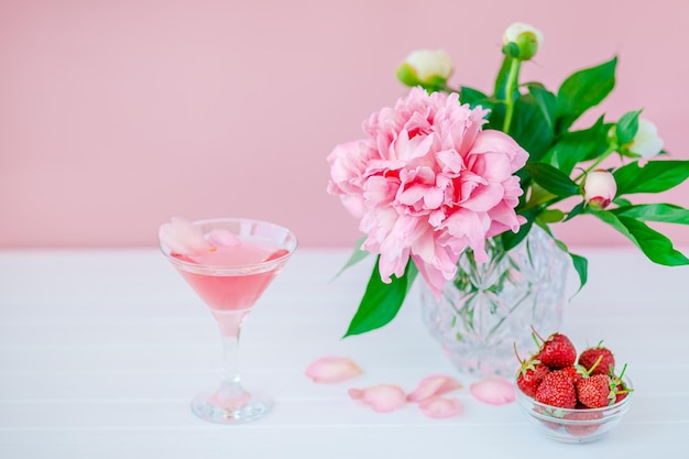 Buon giorno. Peonie rosa in un vaso di cristallo su uno sfondo di legno rosa, copia spazio, primo piano.