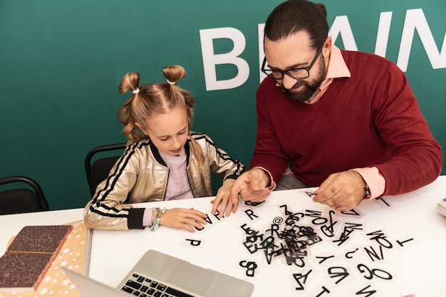 Buon lavoro. Insegnante adulto barbuto dai capelli scuri che indossa occhiali che sembra eccitato mentre mostra nuove parole al suo allievo