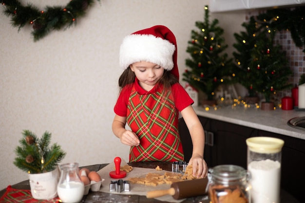 Buon Natale Bambina carina fa i biscotti di Natale nella sua cucina decorata Luci e un albero di Natale Stile di vita Spazio per il testo