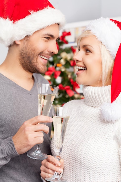 Buon Natale! Bella giovane coppia che tiene flauti da champagne e si guardano l'un l'altro