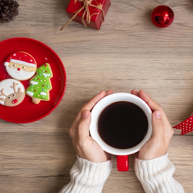 Buon Natale con la mano della donna che tiene la tazza di caffè e il biscotto fatto in casa sul tavolo Festa della vigilia di Natale e concetto di felice anno nuovo