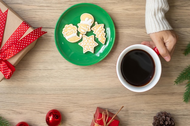 Buon Natale con la mano della donna che tiene la tazza di caffè e il biscotto fatto in casa sul tavolo Festa della vigilia di Natale e concetto di felice anno nuovo
