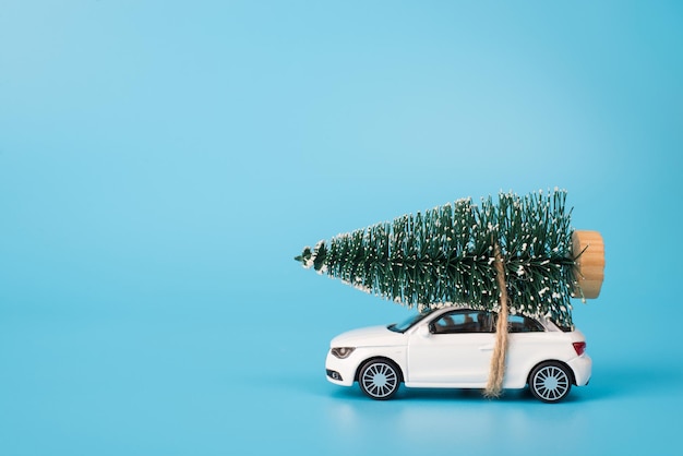 Buon Natale concetto. Profilo laterale foto ravvicinata di mini giocattolo bianco elegante auto moderna che trasportano abete nella neve sulla sommità del tetto isolate su sfondo blu