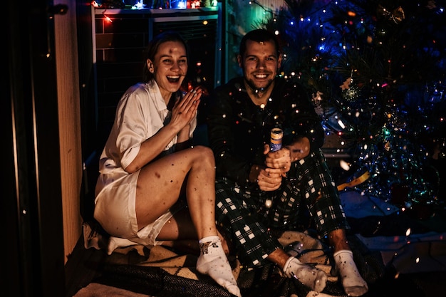 Buon Natale e Buon Anno Nuovo Una giovane coppia innamorata che celebra Natale o Capodanno a casa Una coppia romantica in pigiama che si diverte con i confetti a casa