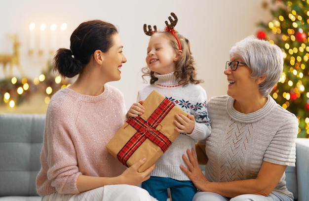 Buon Natale e buone feste! Bambino allegro che presenta regali a mamma e nonna.