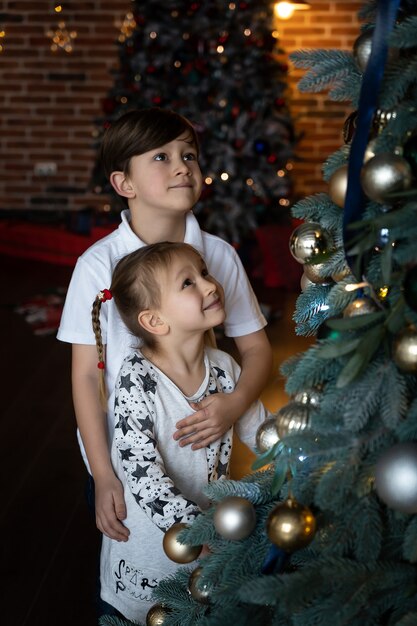 Buon Natale e Buone Feste. Carino bambina e ragazzo sta decorando l'albero di Natale al chiuso.