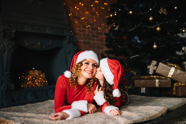 Buon Natale e Buone Feste! La bella madre con la piccola figlia in costumi di Natale trascorre del tempo insieme vicino all'albero di Natale.