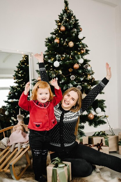 Buon Natale e buone feste La mamma fa un regalo a sua figlia vicino all'albero di Natale Madre allegra che abbraccia una bambina carina insieme a casa Felice anno nuovo 2021