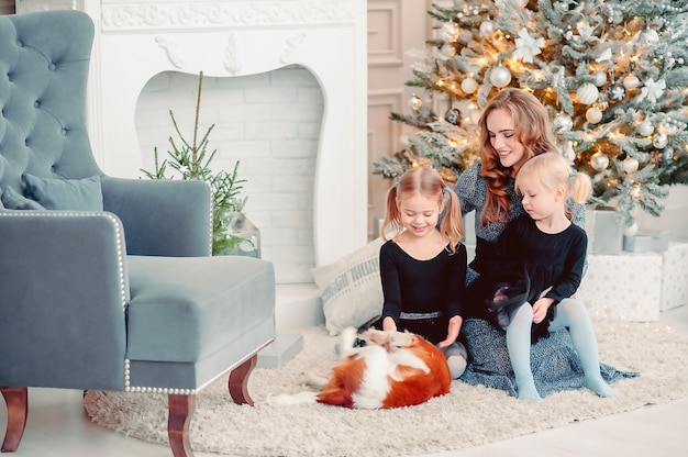 Buon Natale e Buone Feste. mamma e bambini accarezzano il cane, le figlie si divertono vicino all'albero in casa. Famiglia amorevole nella stanza.