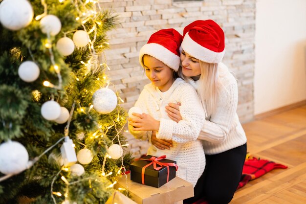 Buon Natale e Buone Feste. Mamma e figlia decorano l'albero di Natale in camera. Famiglia amorevole al chiuso.