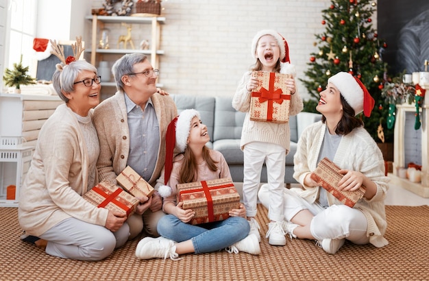 Buon Natale e Buone Feste! Nonna, nonno, mamma e bambini che si scambiano regali. Genitori e figlie che si divertono vicino all'albero al chiuso. Famiglia amorevole con regali in camera.