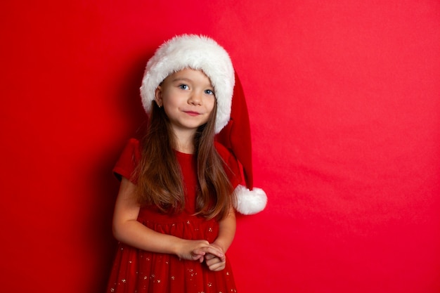 Buon Natale e buone feste Ritratto di una ragazza con un berretto da Babbo Natale su uno sfondo rosso Bambini