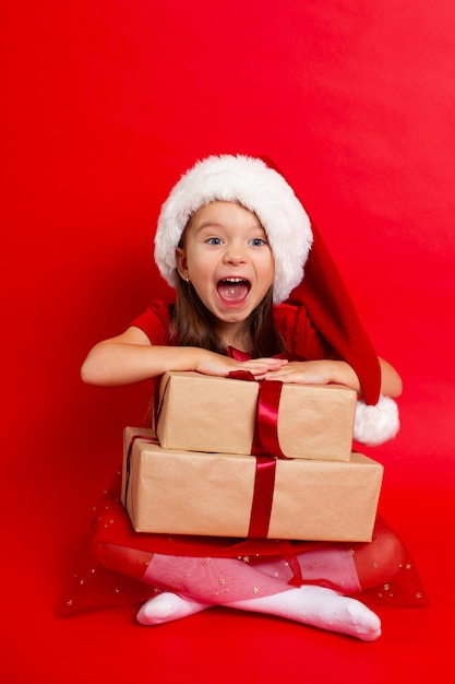 Buon Natale e buone feste Ritratto di una ragazza emotiva con un berretto da Babbo Natale su uno sfondo rosso