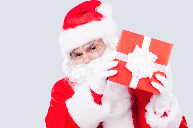 Buon Natale e Felice Anno nuovo! Babbo Natale tradizionale che tiene in mano una scatola regalo e guarda la telecamera mentre è in piedi su uno sfondo grigio