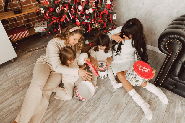 Buon Natale e Felice Anno nuovo! Due donne con le loro giovani figlie sono sedute sul pavimento vicino all'albero di Natale e aprono i regali.