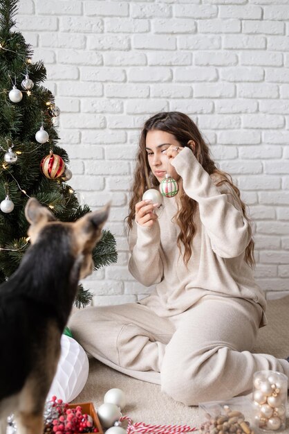 Buon Natale e Felice Anno nuovo. giovane donna attraente che decora l'albero di Natale e gioca con i cani