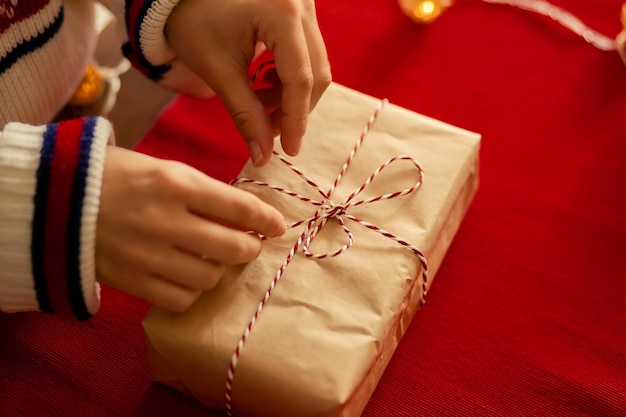 Buon Natale e Felice Anno nuovo. Le mani delle donne legano un nastro su un regalo su uno sfondo rosso