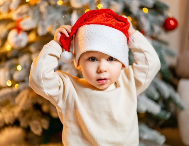 Buon Natale e Felice Anno Nuovo Ritratto di un bambino che indossa un cappello da Babbo Natale Bambino gioioso che guarda l'obbiettivo a Natale nel soggiorno di casa