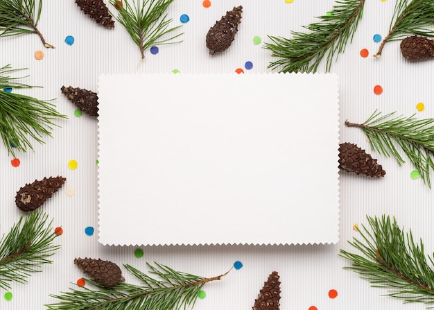 Buon Natale e felice anno nuovo sfondo. Foglio di carta per appunti bianco. Decorazioni da rami di pino, pigne e coriandoli festivi