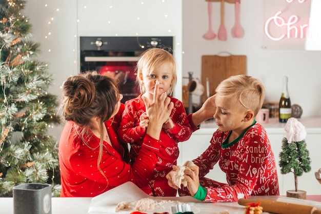 Buon Natale. Mamma e bambini fanno i biscotti di Natale, sporcandosi di farina, in rosso