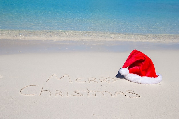 Buon Natale scritto sulla sabbia bianca della spiaggia tropicale con cappello di Natale