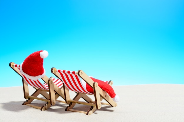 Buon Natale sul concetto di spiaggia. Due sedie a sdraio con cappelli di Babbo Natale