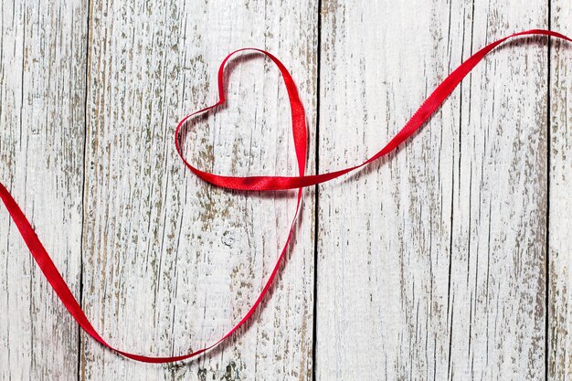 Buon San Valentino. Cuore del nastro rosso su fondo di legno bianco.