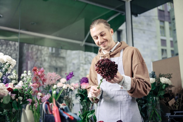 Buon umore. Giovane allegro che mantiene il sorriso sul suo volto mentre guarda il fiore