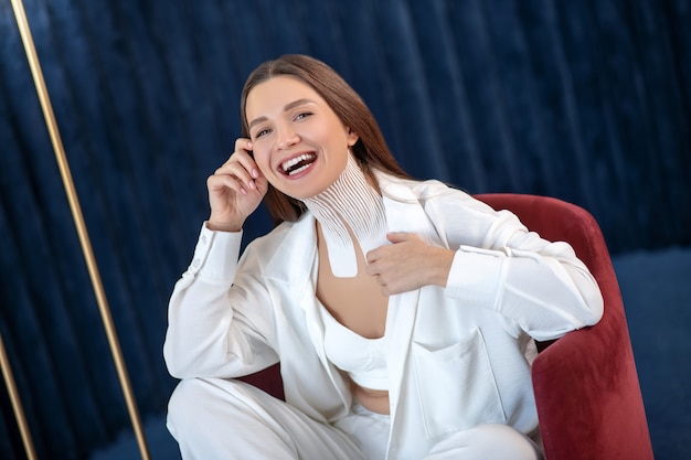 Buon umore. Giovane donna con nastri sul collo seduto su una sedia e guardando allegra