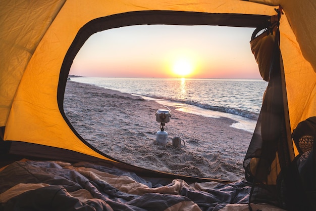 Buon viaggio - vista sul mare, bruciatore, bombetta, tazza dalla tenda gialla sulla spiaggia all'alba. Paesaggio ucraino al Mar d'Azov, Ucraina