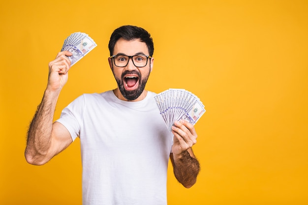 Buon vincitore! Giovane uomo ricco in banconote da un dollaro di denaro azienda casual con sorpresa isolato su sfondo giallo.