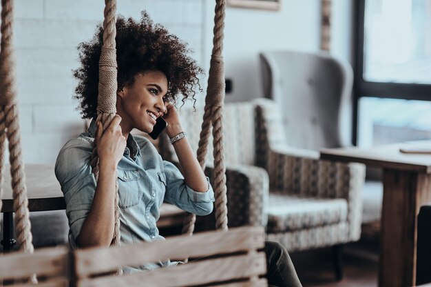 Buona chiacchierata con l'amico. Bella giovane donna africana che parla sullo smart phone e sorride