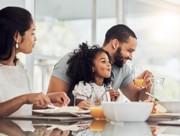 Buona colazione in famiglia e mangiare a tavola a casa parlando o discutendo insieme Ama il sostegno e l'uomo comico donna e bambina che ridono cura e legame bevono succo d'arancia e mangiano