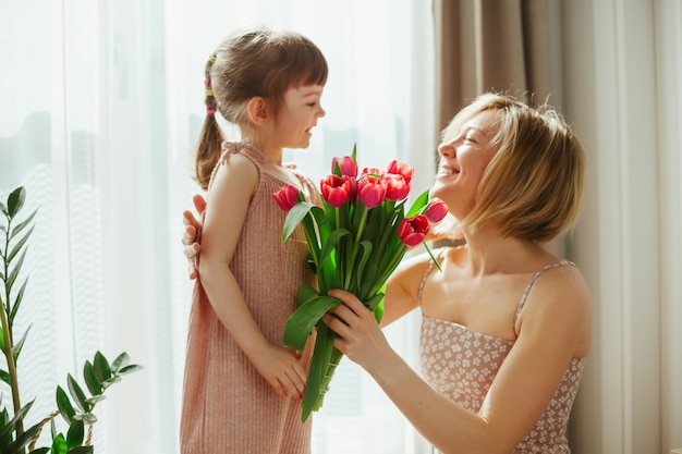 Buona festa della mamma! Bambina che si congratula con sua madre e le dà dei fiori. Mamma e figlia che sorridono e trascorrono del tempo insieme. Concentrati sui tulipani.