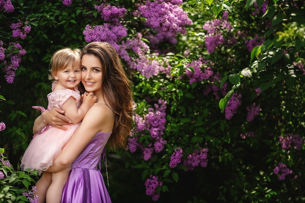 Buona festa della mamma! copia spazio. La bella giovane donna e la sua piccola figlia affascinante stanno abbracciando e sorridendo. Alberi fioriti