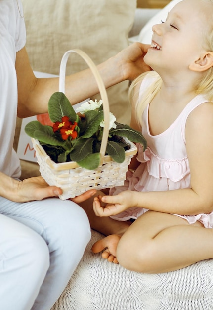 Buona festa della mamma! La figlia del bambino si congratula con la mamma e le dà il cesto di fiori primaverili e la cartolina con il disegno del cuore. Concetti di famiglia e infanzia.