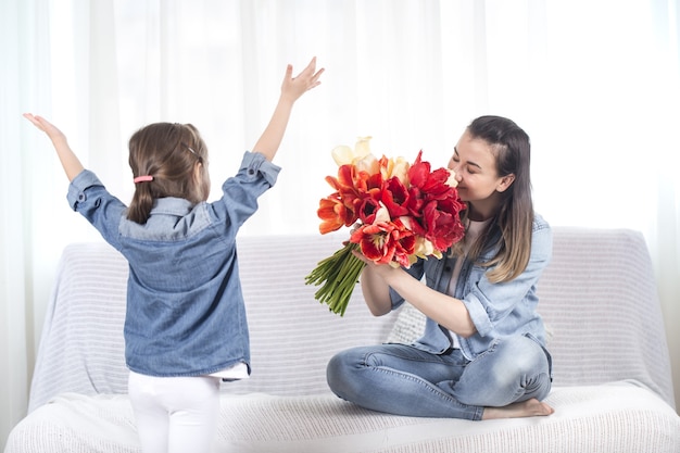 Buona festa della mamma. La piccola dolce figlia con un grande mazzo di tulipani si congratula con sua madre. All'interno del soggiorno, il concetto di una vita familiare felice