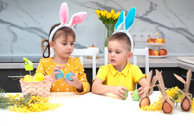 Buona Pasqua bambini divertenti con orecchie da coniglio si stanno preparando per le vacanze Un bambino un ragazzo e una ragazza indossano orecchie da coniglio e giocano con uova colorate