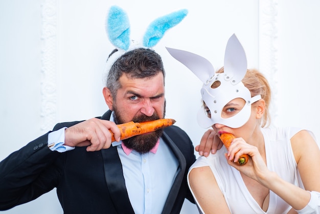 Buona Pasqua e divertente giorno di Pasqua. Costume da coniglio orecchie da coniglio. Coppie sorprese del coniglietto che portano le orecchie del coniglietto e mangiano la carota.