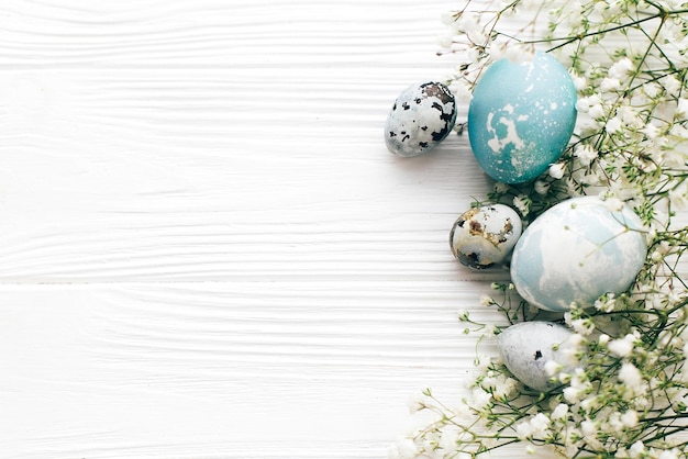 Buona Pasqua Eleganti uova di Pasqua con bordo di fiori primaverili piatto giacevano su fondo di legno bianco con spazio per il testo Uova di Pasqua moderne dipinte con colorante naturale in marmo blu e grigio