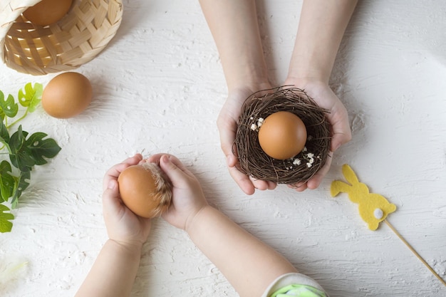 Buona Pasqua Le mani dei bambini tengono le uova di Pasqua in un piccolo nido su un tavolo bianco Decorazione dell'uovo