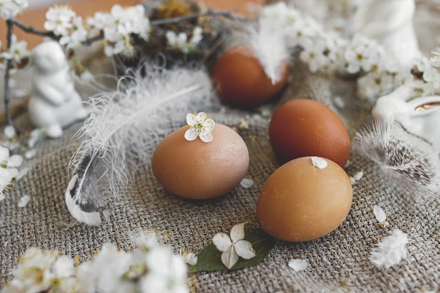 Buona Pasqua Le uova di Pasqua con petali bianchi nidificano le piume dei coniglietti sul tovagliolo di lino rustico