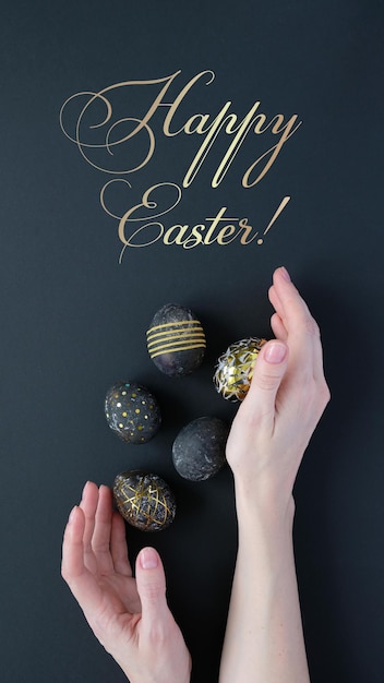 Buona Pasqua. Mani di donna che tengono le uova di Pasqua nere con motivo oro su sfondo nero. Pasqua di lusso