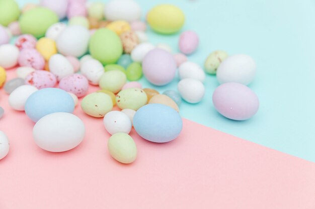 Buona Pasqua. Preparazione per le vacanze. Uova di cioccolato della caramella di Pasqua e dolci del jellybean isolati sul rosa blu pastello d'avanguardia. Semplice spazio minimalista piatto vista dall'alto copia spazio.