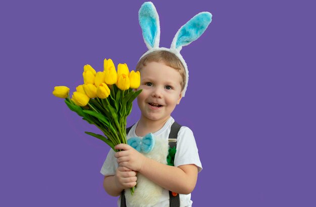Buona Pasqua Un bambino in costume da coniglio tiene in mano un mazzo di tulipani gialli È tempo di caccia alle uova Un bambino affascinante con divertenti orecchie da coniglio Primavera Pasqua Il concetto di un'infanzia felice